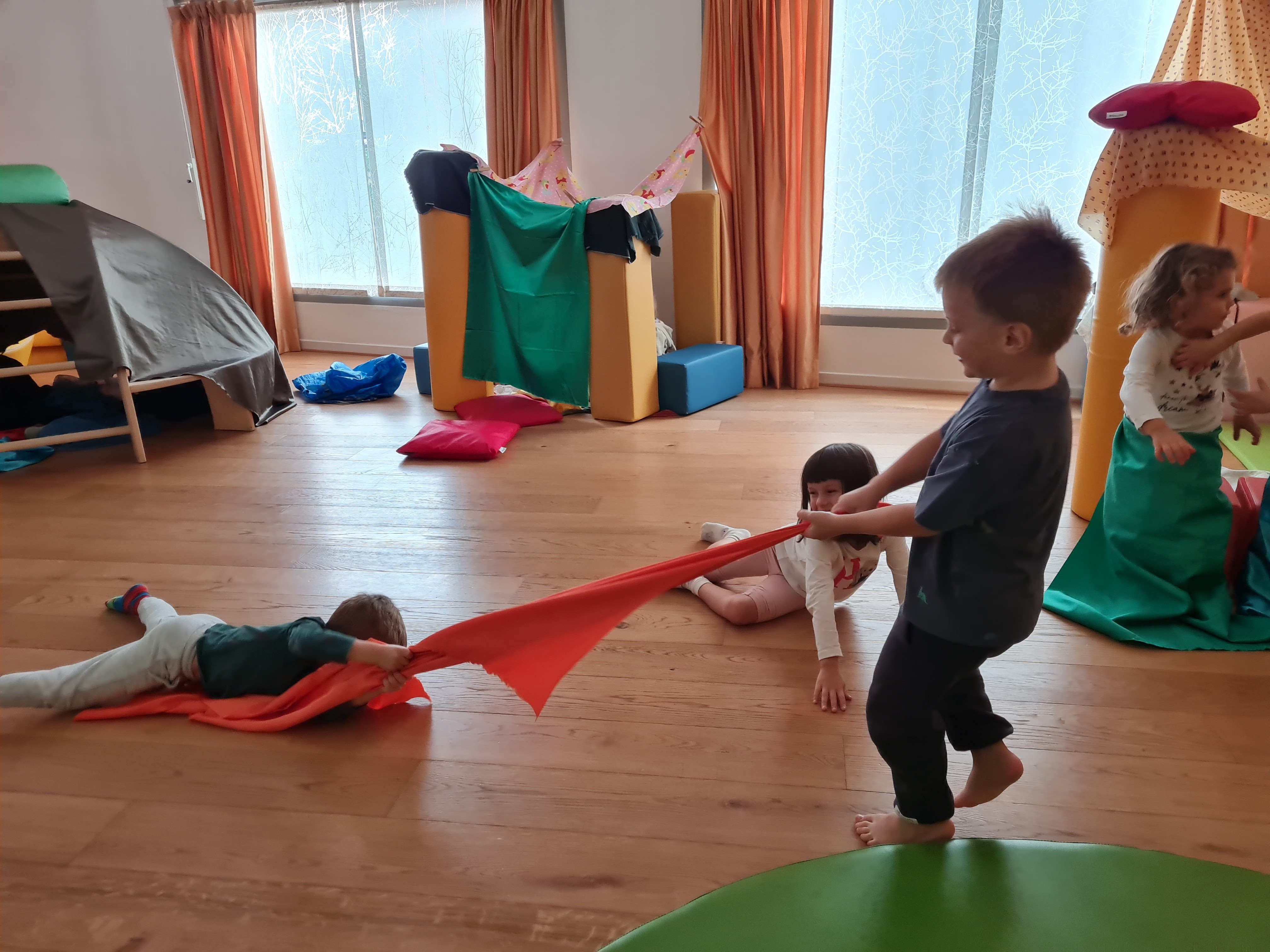 Bambini che giocano tirando un telo rosso nella sala