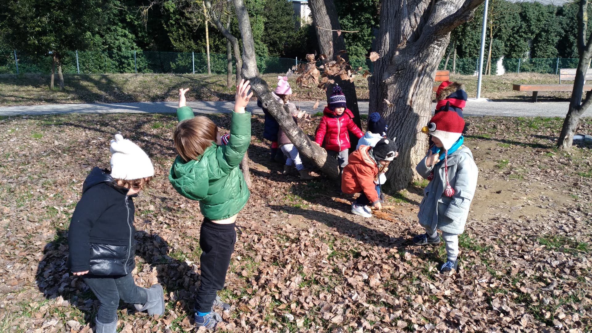 Bambini con il cappello che giocano tra le foglie secche sotto un albero in un parco d’inverno
