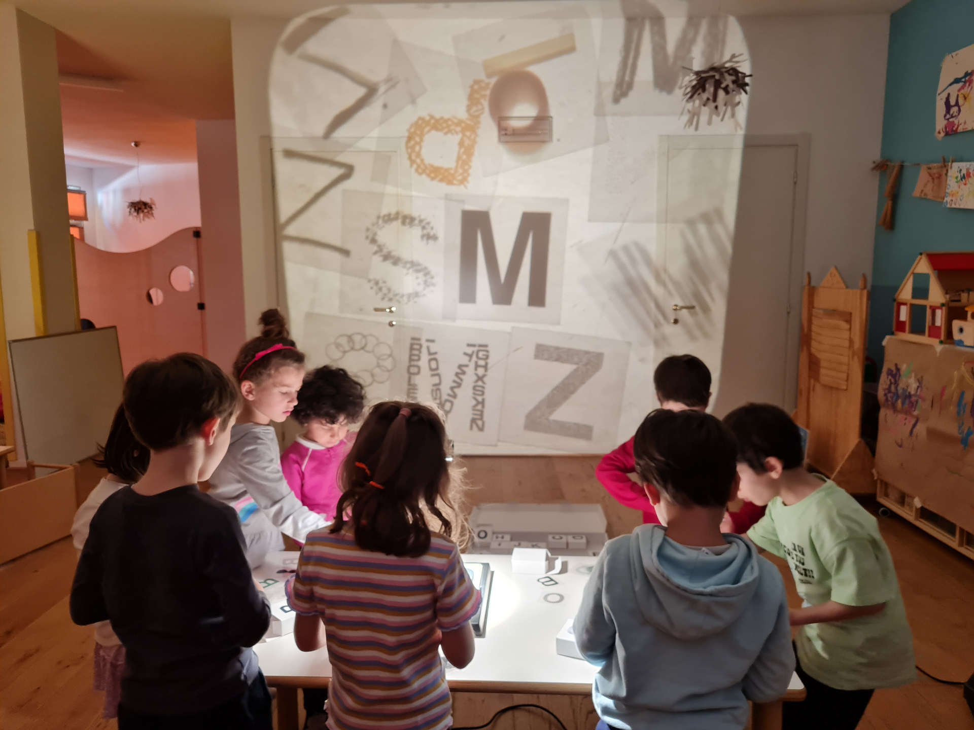 Bambini attorno a un tavolo luminoso con lettere proiettate sulla parete