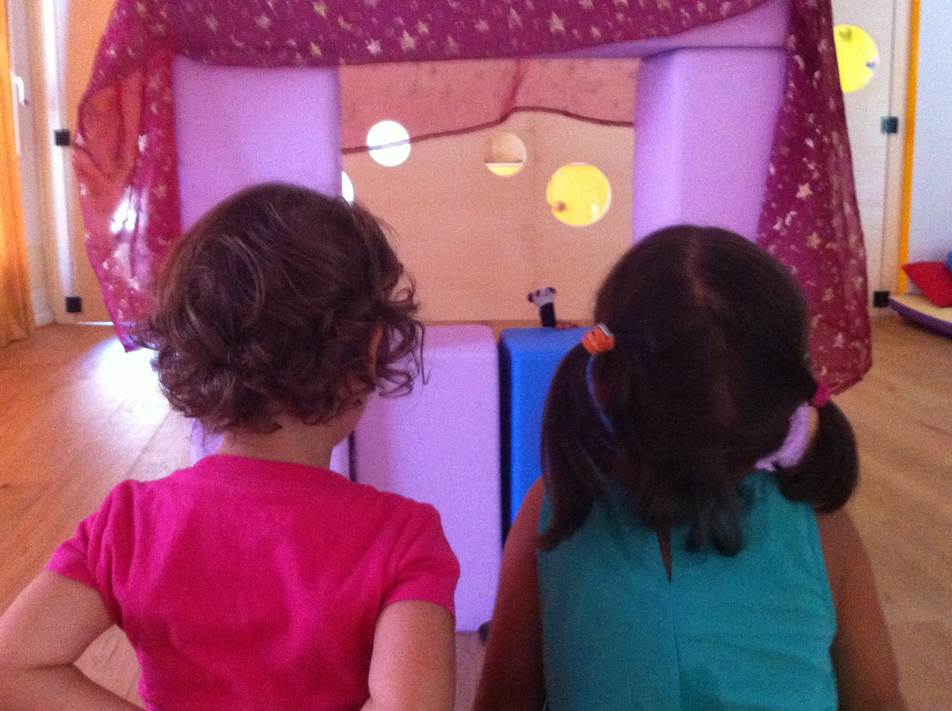 Due bambini visti da davanti una casetta morbida con tende rosa e blocchi colorati nella sala del gioco