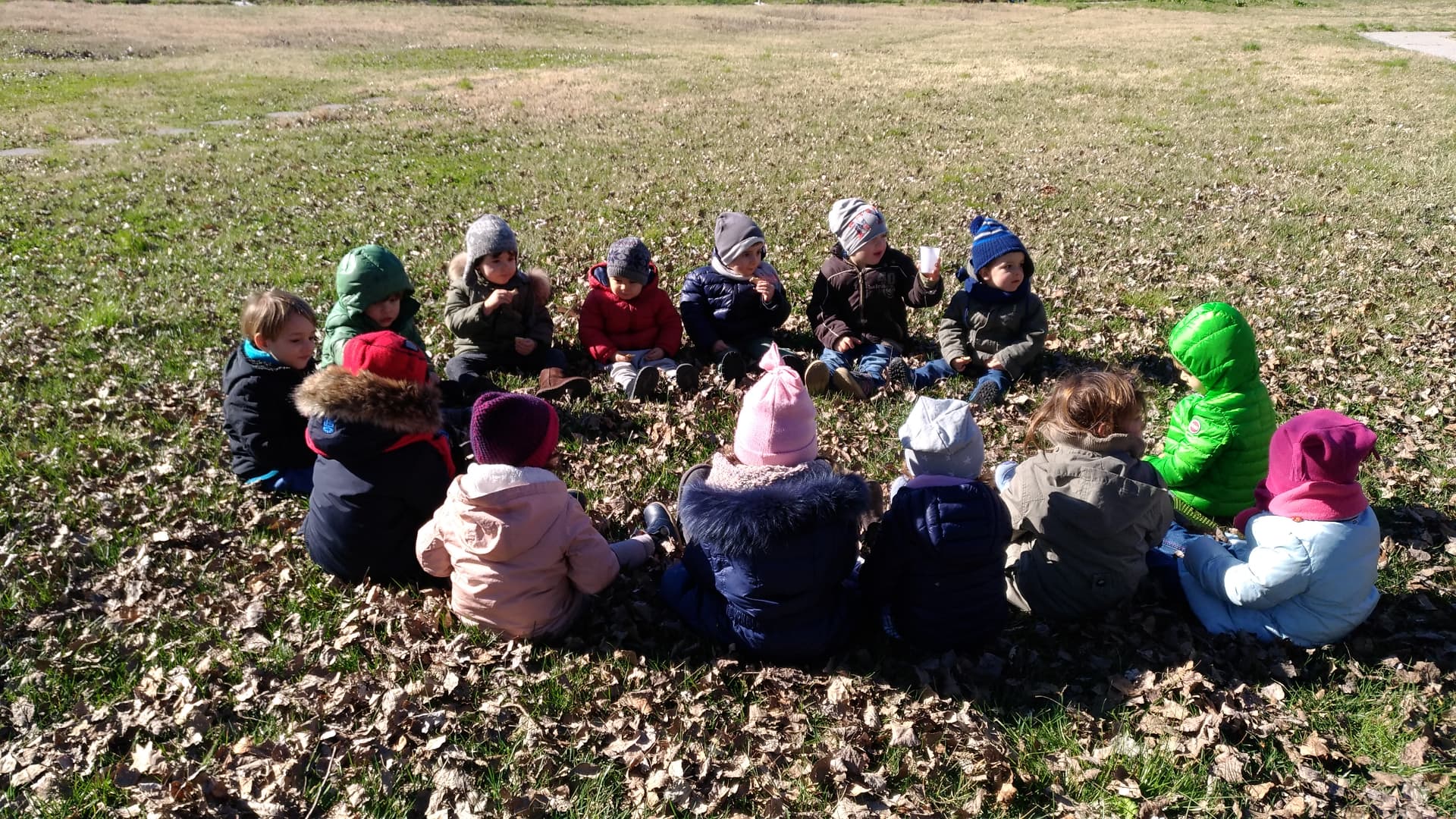 Bambini con cappelli e giacche colorate seduti in cerchio sul prato di un parco