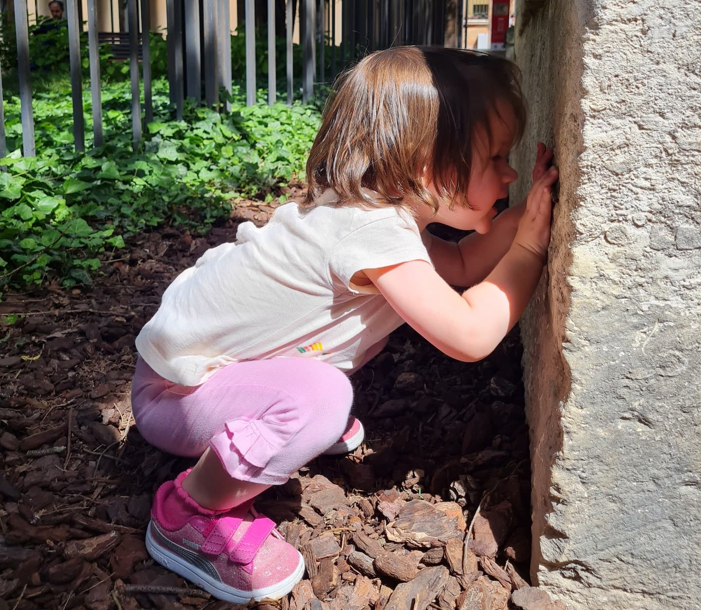 Bambina accovacciata che tocca un muro di pietra durante una passeggiata all’aperto