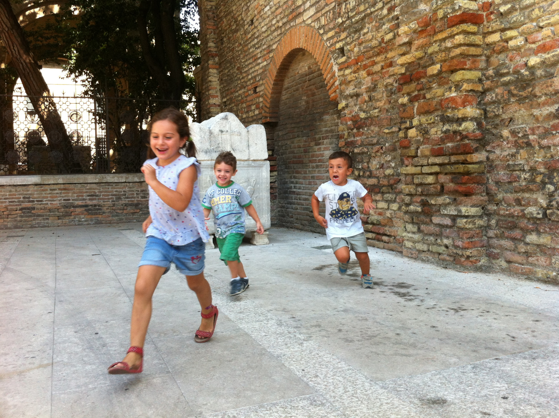 Tre bambini che corrono ridendo in un cortile di mattoni antichi